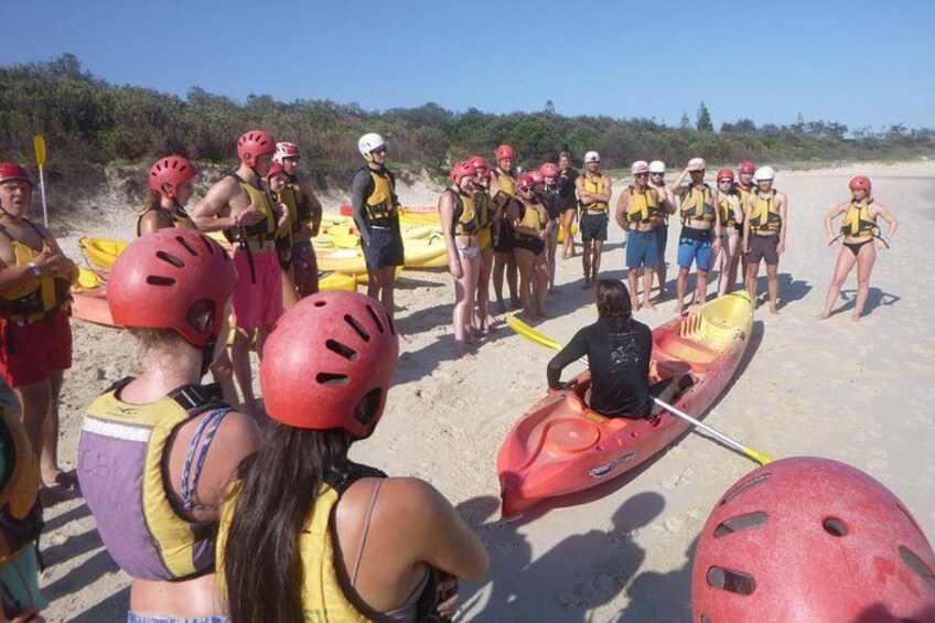 A group of people in a red kayak on a sandy beach, wearing helmets and life jackets. 3