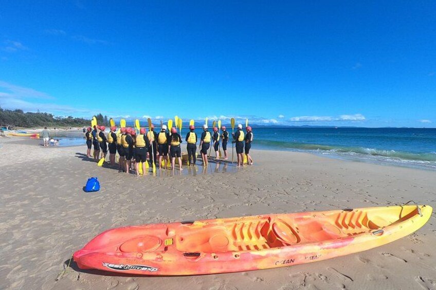 A group of people on a beach with a kayak in the foreground. 2