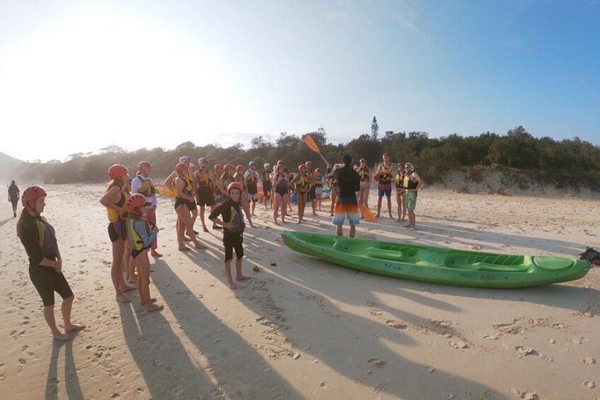 Un groupe de personnes se trouve sur une plage, près d’un kayak vert. 2