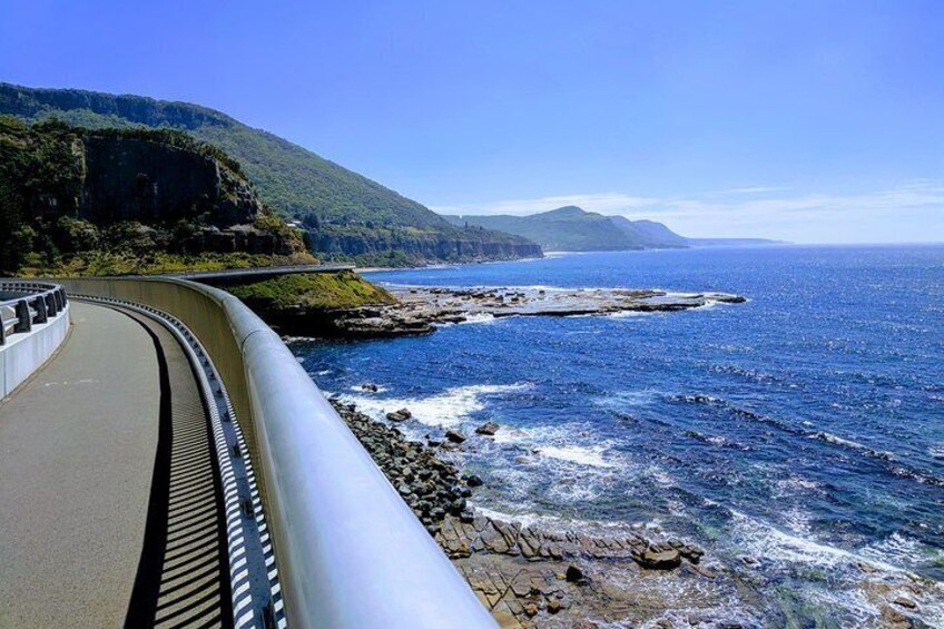 A coastal road curving along a rocky shoreline with a view of the ocean and distant mountains. 2