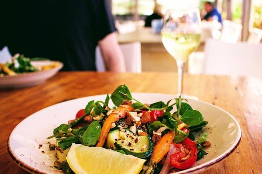 A plate of food with a lemon wedge, greens, and vegetables on a wooden table. 3