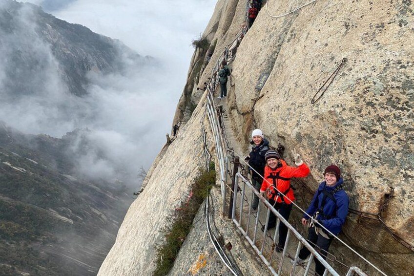 A group of people on a mountain trail with rocky terrain and a misty valley in the background. 2