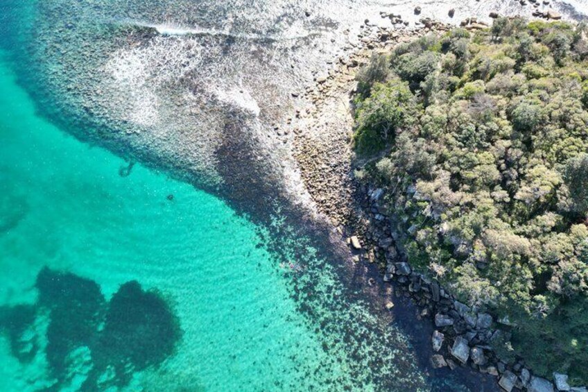 Eine Küstenlandschaft mit klarem türkisblauem Wasser, einer felsigen Küstenlinie und üppiger grüner Vegetation. 2