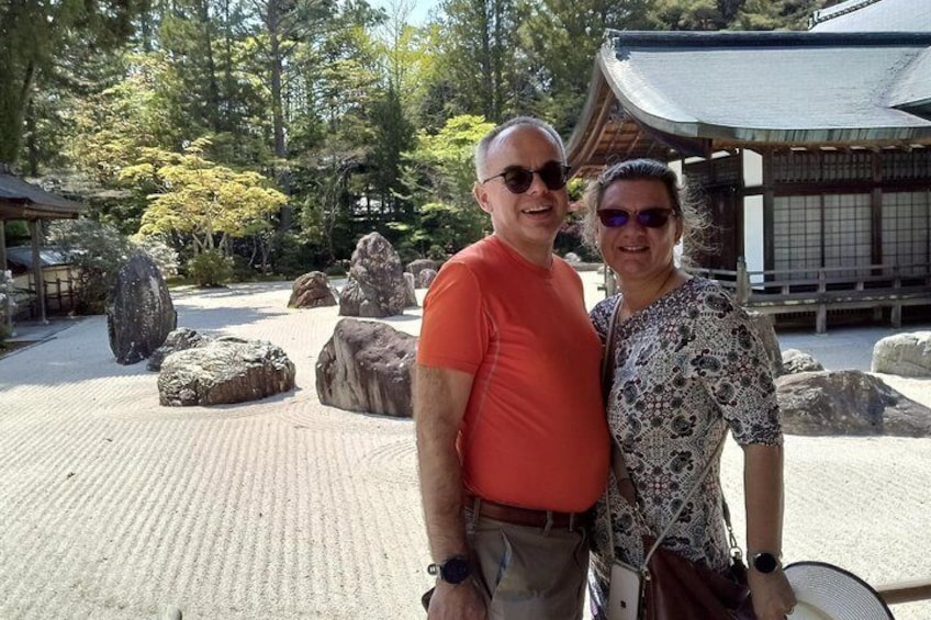 Two people standing in a garden with large rocks and a traditional Japanese building in the background. 4