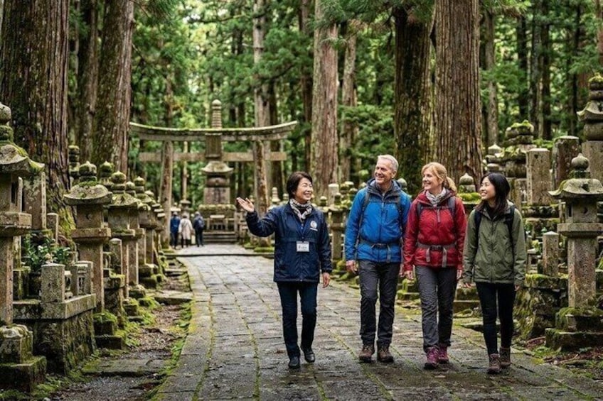 A group of people walking through a forested area with stone lanterns and a traditional Japanese torii gate. 1