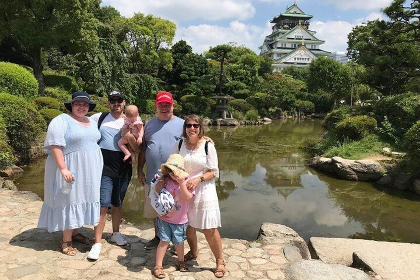 Una familia de cinco personas en un parque con un estanque y un castillo al fondo. 4