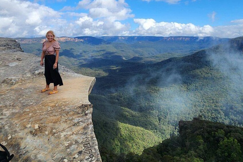 A person standing on a concrete ledge overlooking a valley with dense green vegetation and distant mountains. 2