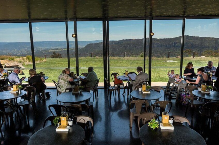 Un restaurante con mesas y sillas, ventanas amplias y vistas a un paisaje verde. 5