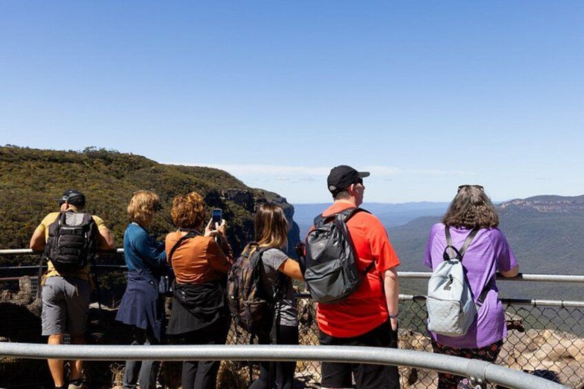 Un grupo de personas de pie en una plataforma panorámica, contemplando un paisaje montañoso. 3