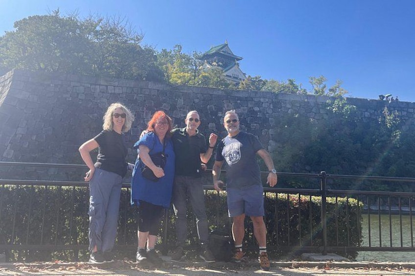 A group of people standing in front of a stone wall with a traditional Japanese building in the background. 1