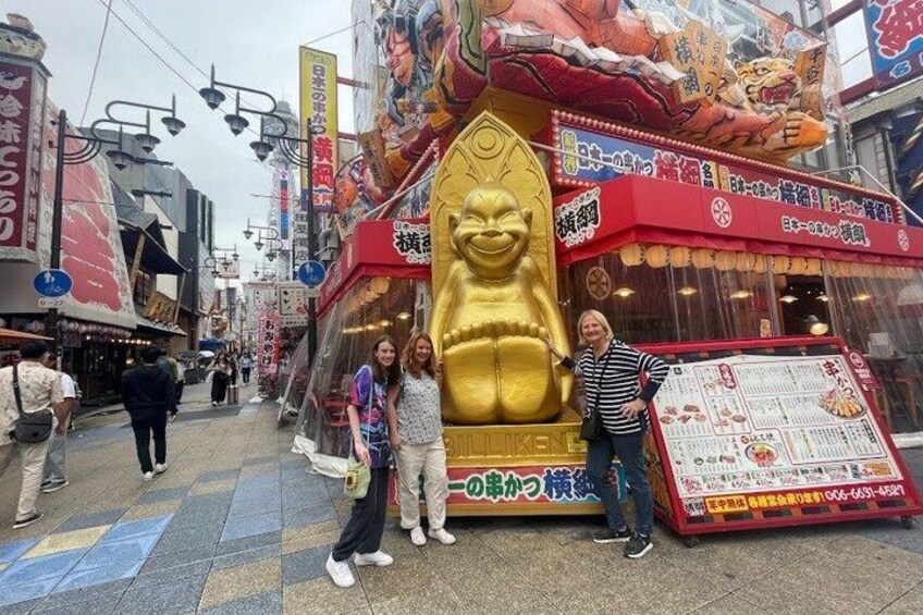 Une rue avec une grande statue dorée, des passants et un panneau indicateur. 3