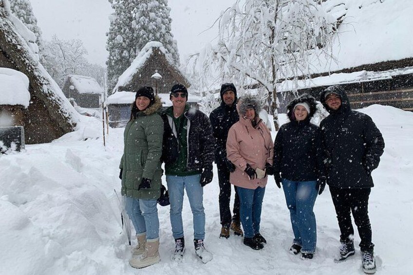 Un groupe de personnes se tient debout dans un paysage enneigé, avec des arbres et des maisons couverts de neige. 3