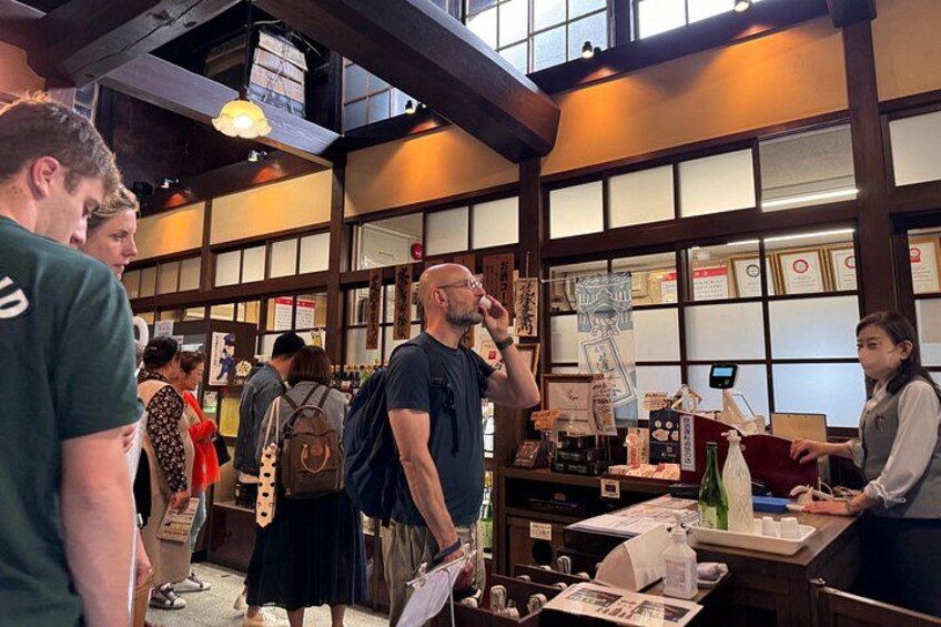 L’intérieur d’une maison de thé japonaise traditionnelle, avec un sol recouvert de tatamis, des paravents shoji et un comptoir où une personne sert du thé. 2