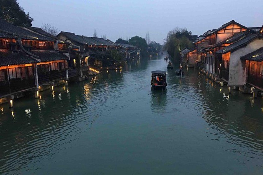 A river with traditional buildings on either side, a boat in the water, and a person standing on a bridge. 3