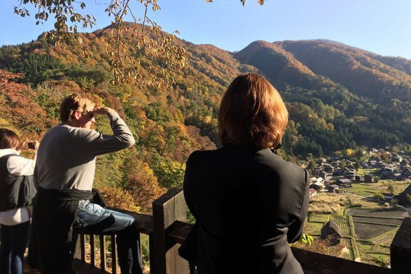 A person taking a photograph of a mountainous landscape with a village below. 3