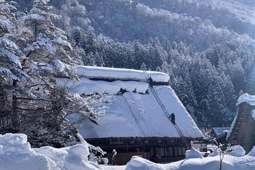 Una casa cubierta de nieve con gente removiendo nieve del techo. 2