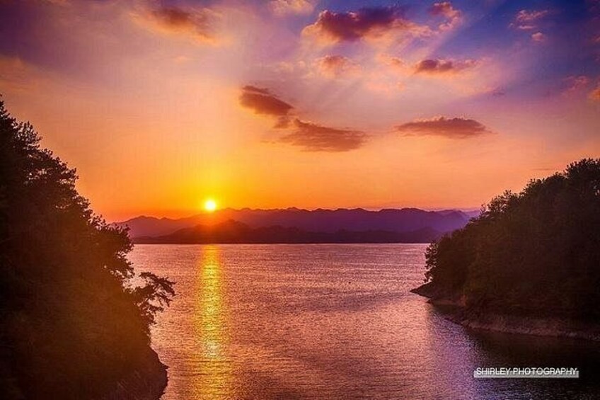 A sunset over a calm body of water with trees on either side. 5