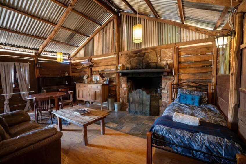 Interior rústico de una cabaña con una mesa de comedor de madera, un sofá, una chimenea y una cama. 2