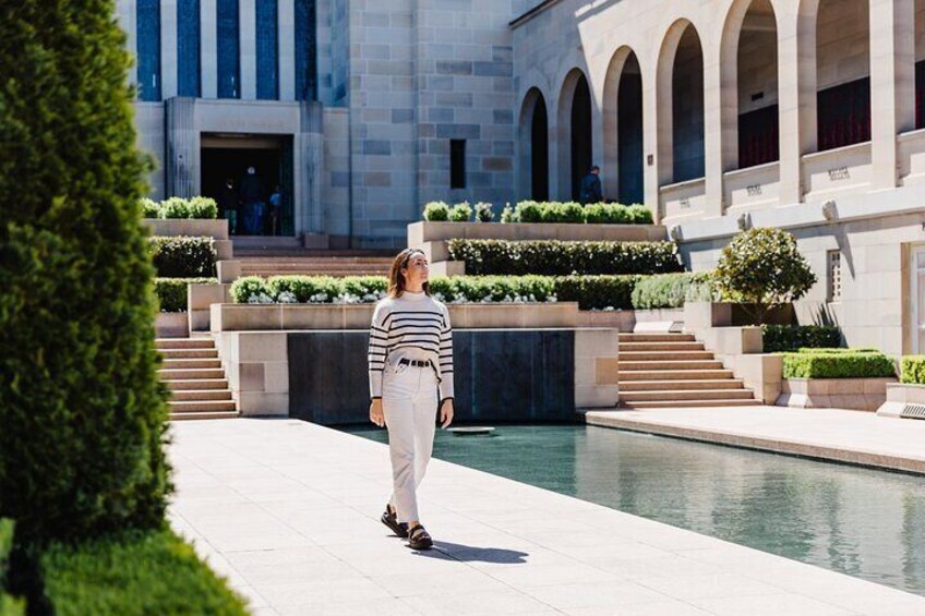 A person walking on a pathway in a courtyard with a pool and a building with arches in the background. 1