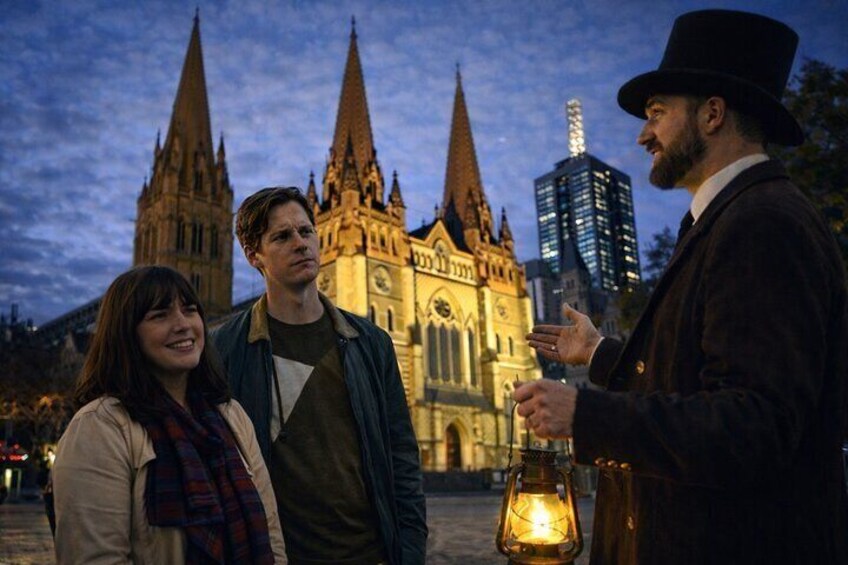 Three people standing in front of a cathedral with spires, a modern building, and a street lamp. 2