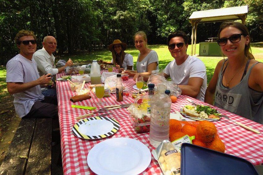 Een groep mensen zit buiten aan een picknicktafel met eten en drinken. 2