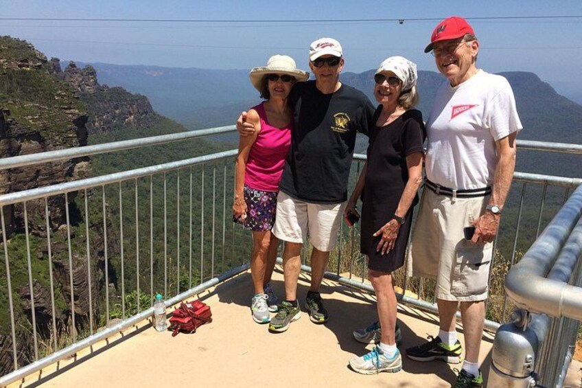 A group of people standing on a viewing platform with a mountainous landscape in the background. 3