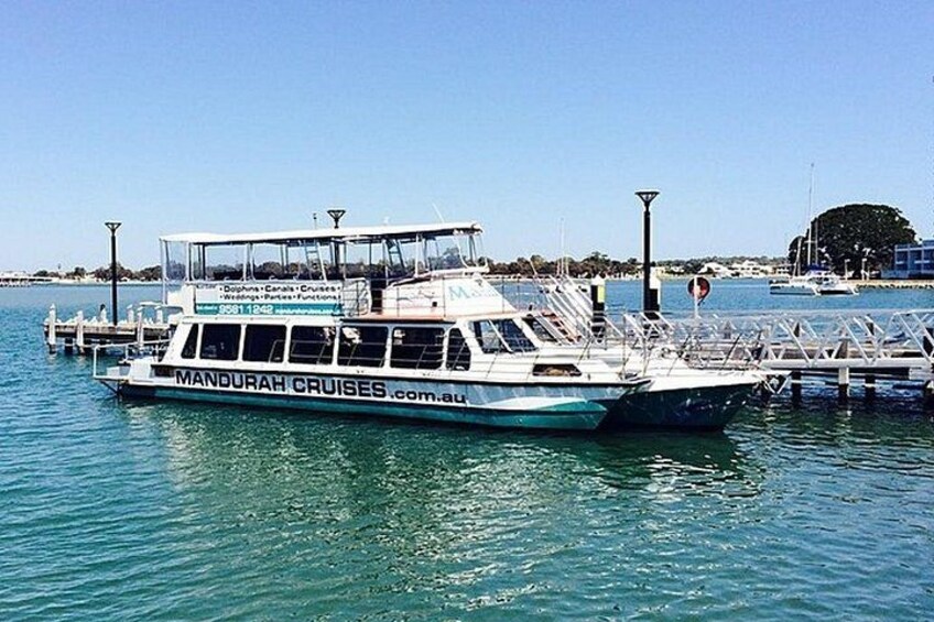 A boat named 'MANDURAH CRUISES' docked at a pier with clear blue water and a calm sea. 4