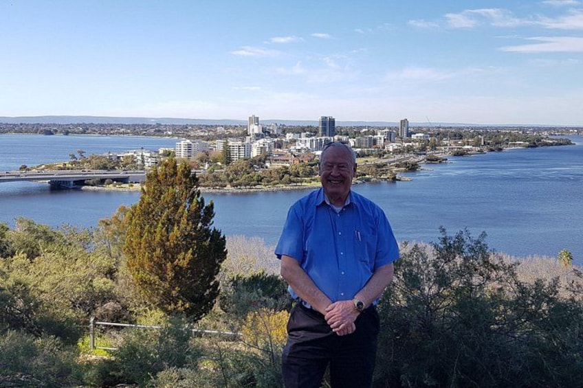 A man standing in a natural setting with a cityscape in the background. 3