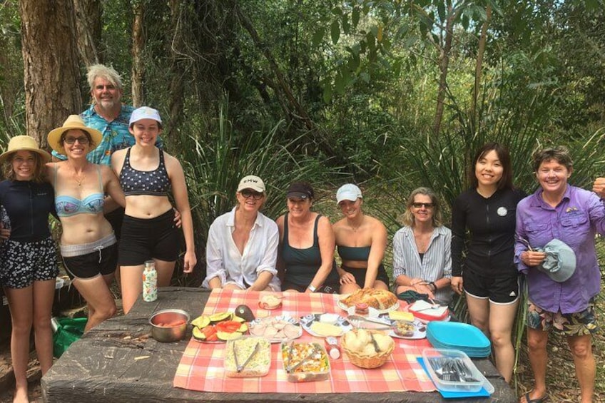 Un grupo de personas reunidas alrededor de una mesa de picnic con comida y bebidas en una zona boscosa. 2