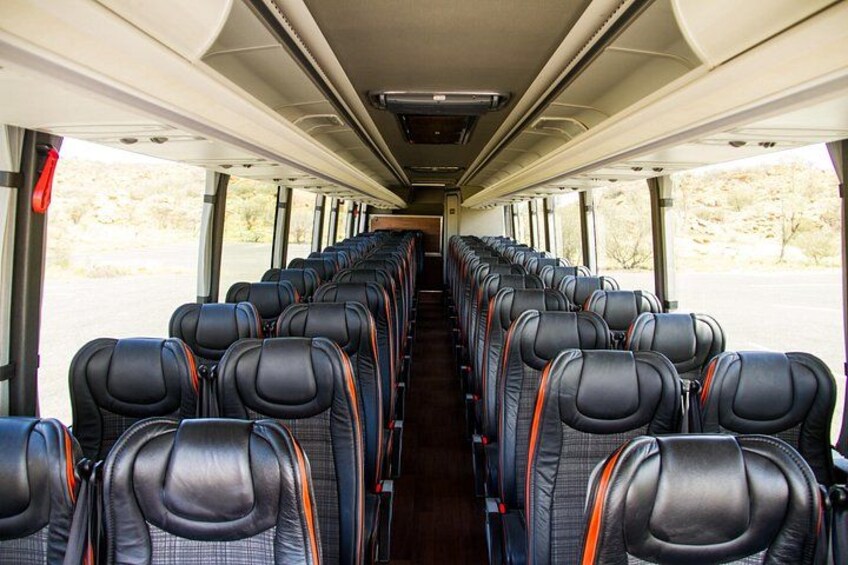 Interior de autobús con asientos de cuero negro en hileras y compartimentos superiores. 1