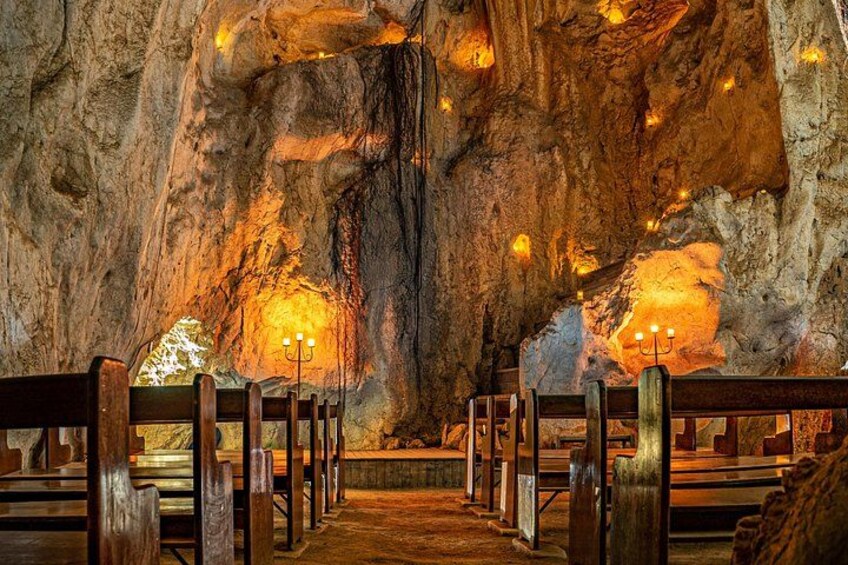 L’intérieur d’une grotte, avec des bancs en bois et des alcôves éclairées par des bougies. 2