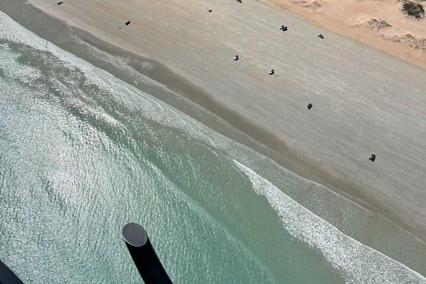 An aerial view of a beach with people walking along the shore and a large cylindrical structure near the water. 2