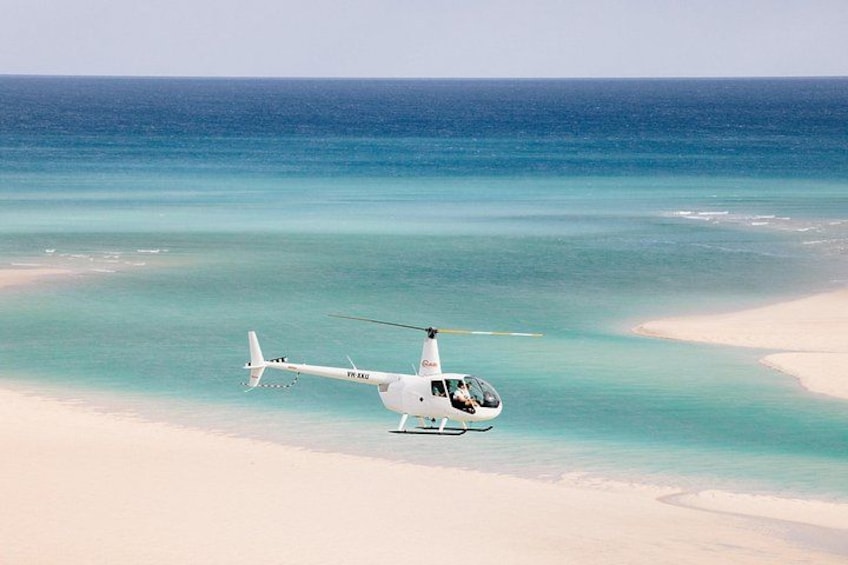 A white helicopter flying over a beach with clear turquoise water. 5