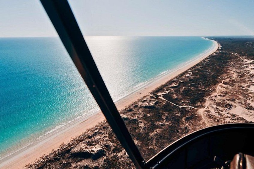 An aerial view of a beach with clear blue water, sandy shore, and sparse vegetation. 3