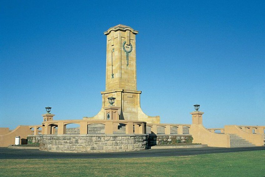 Una torre alta color beige con un reloj, rodeada por un muro de piedra y farolas. 3