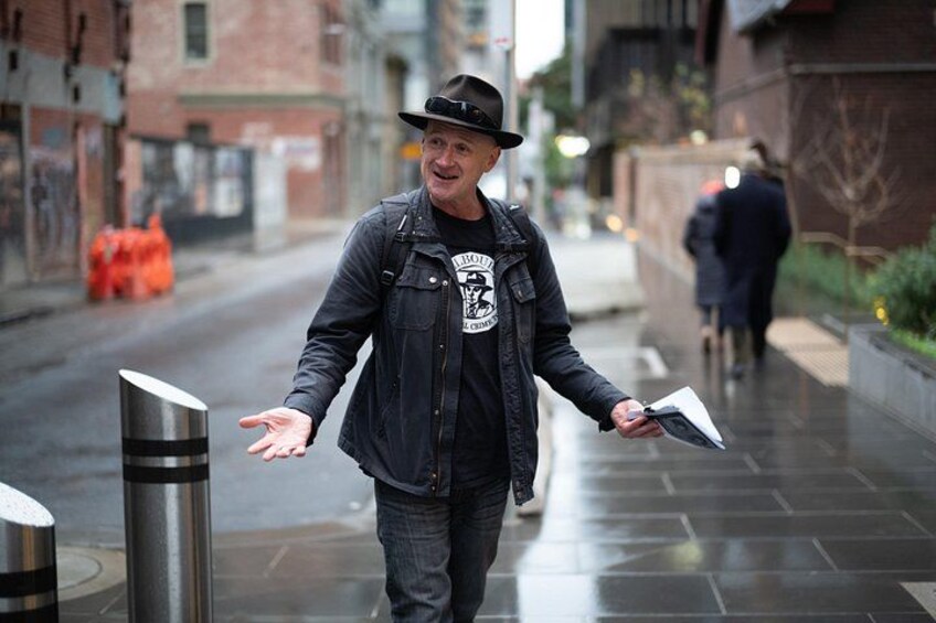A person walking on a wet street with buildings and bollards. 4
