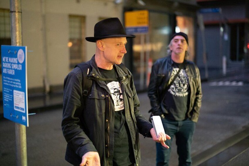 Two people walking on a street, one holding a phone. 1