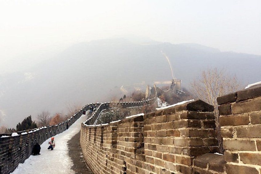 A snow-covered section of the Great Wall of China with a person sitting on the ground. 2
