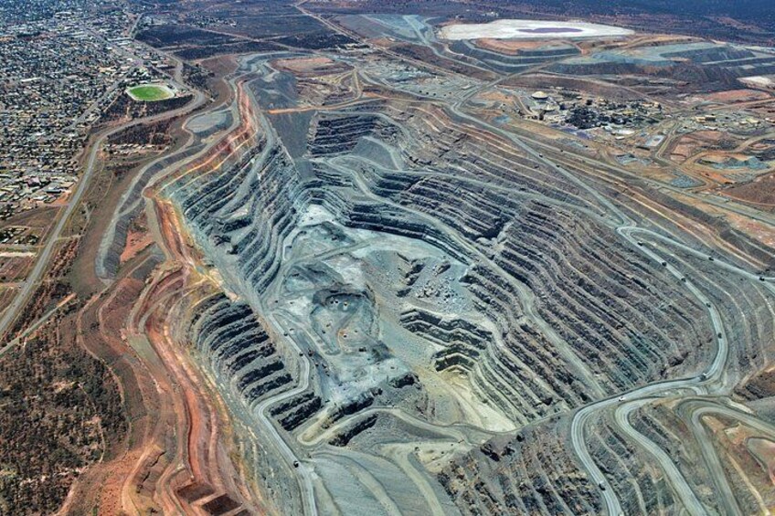 An aerial view of a large open-pit mine with winding roads and visible mining activity. 1