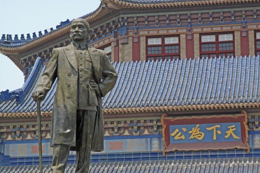 A statue of a man in a suit holding a cane, standing in front of a traditional building with tiled roofs and a sign with Chinese characters. 1