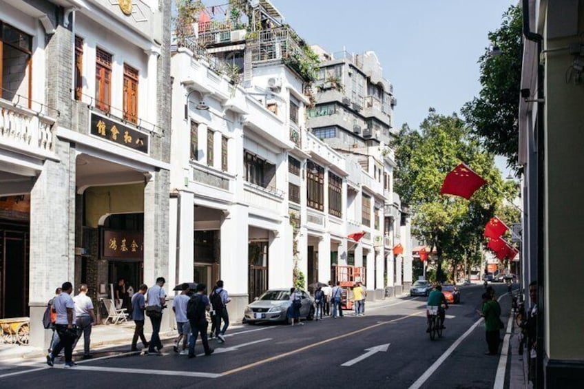 A street with pedestrians, cars, and bicycles. There are buildings with signs and awnings. 2