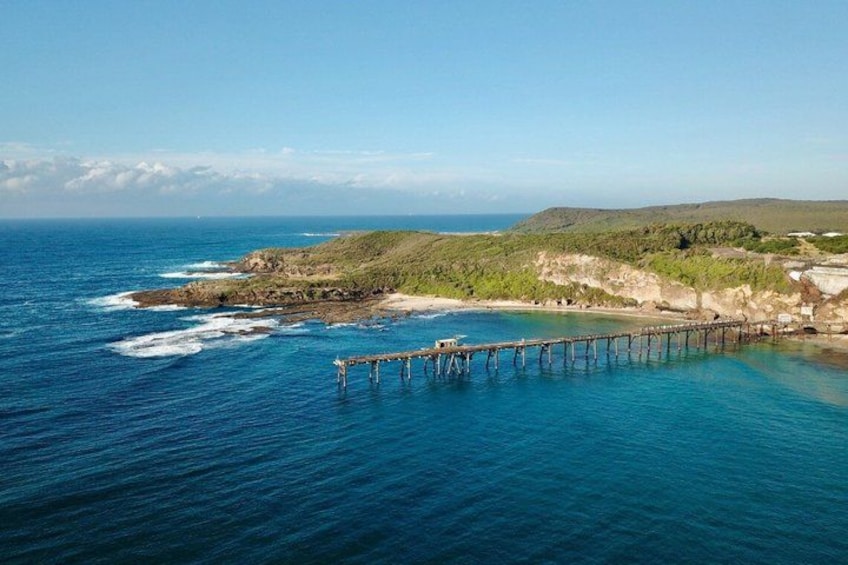 A coastal landscape with a wooden pier extending into the ocean, surrounded by green hills and a clear sky. 2