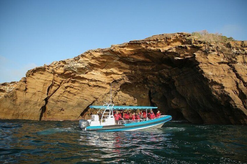 A boat with passengers near a rocky cliff. 1