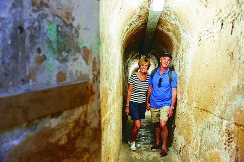 A narrow stone tunnel with a wooden beam on the left and a person in a blue shirt and shorts on the right. 4