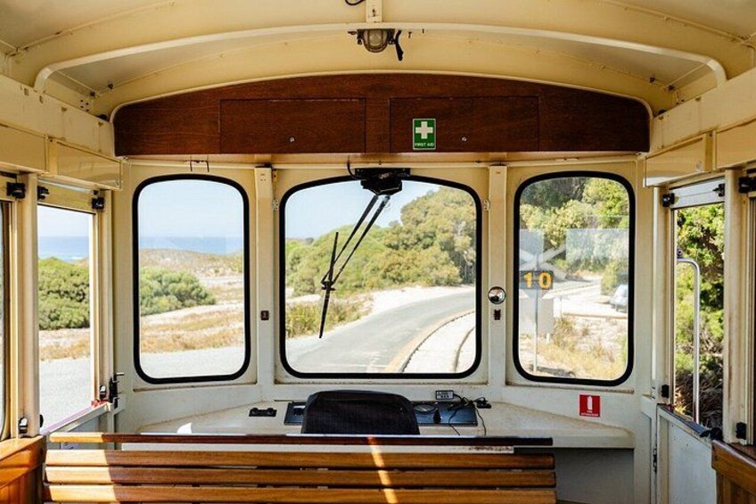 A bus interior with three large windows, a wooden bench, and a green emergency exit sign. 2