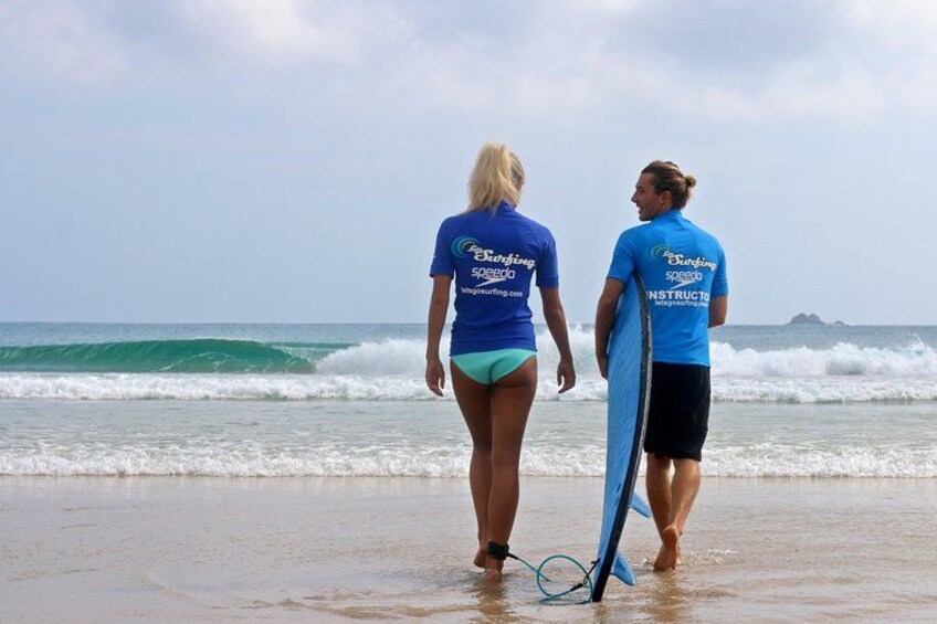 Dos personas caminando por la playa con tablas de surf, olas del océano y una isla distante. 2