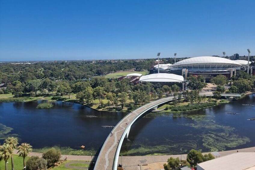 Un estadio con un amplio techo blanco, un puente curvo sobre un río y abundante vegetación circundante. 4