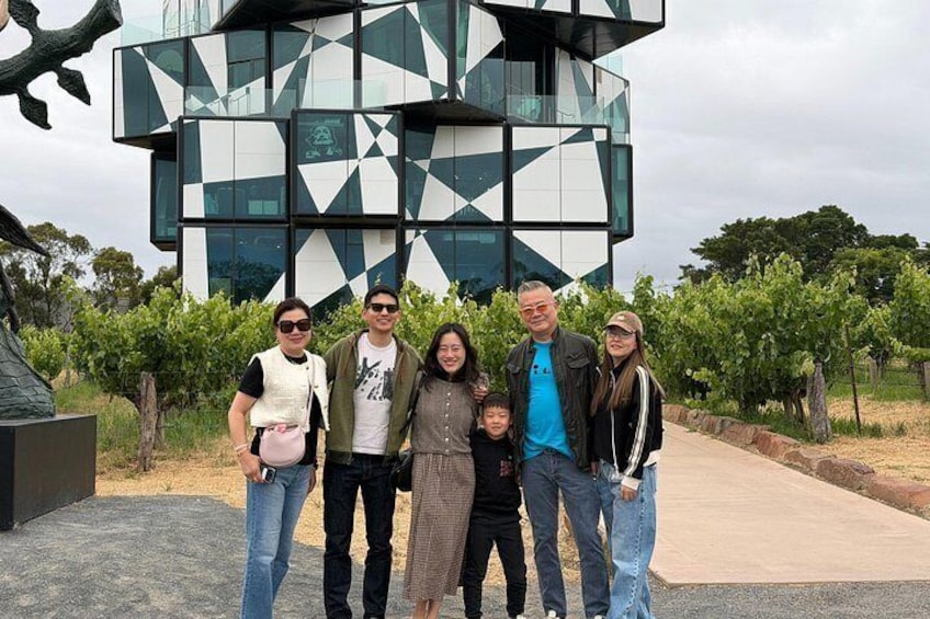 Una familia posando frente a un edificio moderno con diseños geométricos, rodeada de un viñedo. 4