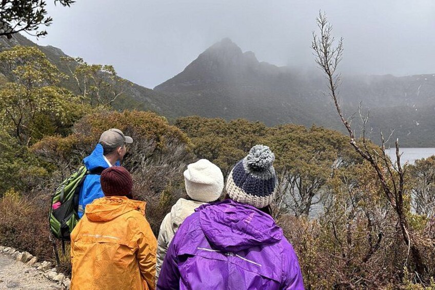 Three people hiking on a trail with a mountainous landscape in the background. 1