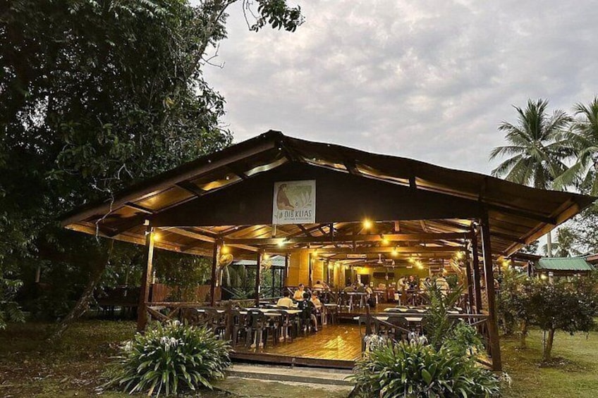 An outdoor dining area with a covered roof, surrounded by greenery and palm trees. 5